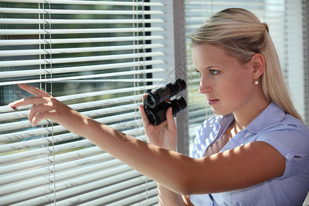 女猎手女人用望远镜透过百叶窗看背景