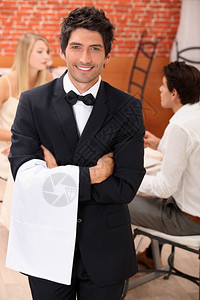 身穿盛装的服务员面对摄影机在一情侣后面在餐厅吃饭背景图片