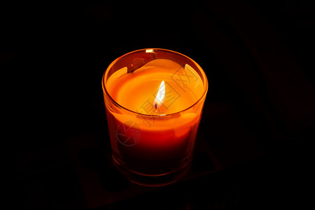 玻璃烛台上的明亮橙色蜡烛在黑暗中燃烧图片