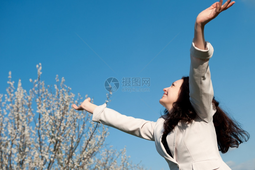 快乐的有魅力女士举起手站在蓝色的天空上图片