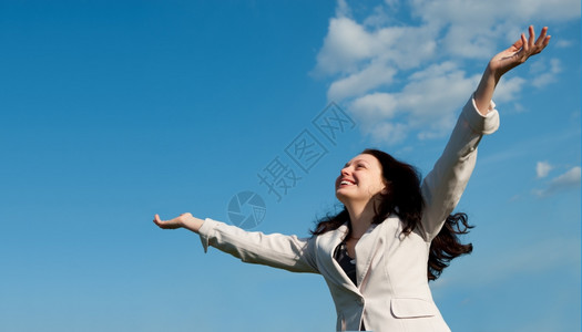 快乐的有魅力女士举起手站在蓝色的天空上图片