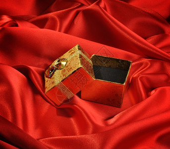 红色丝绸上带有结婚戒指的金色空箱图片