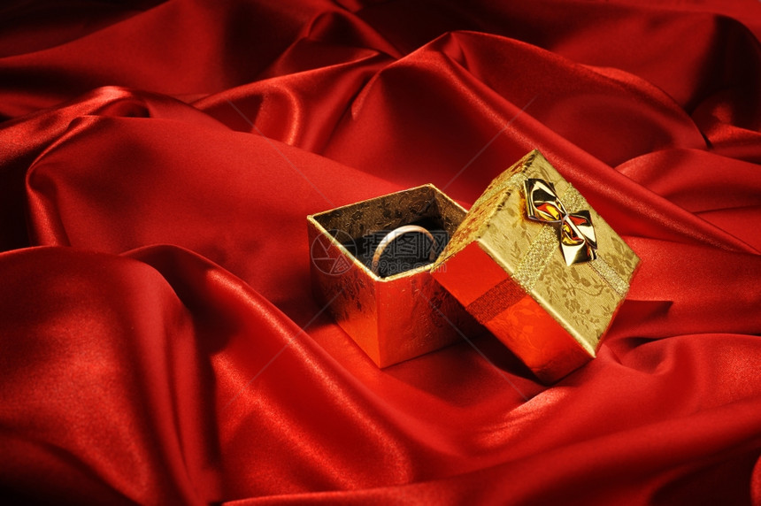 红色丝绸上戴着结婚戒指的金盒图片