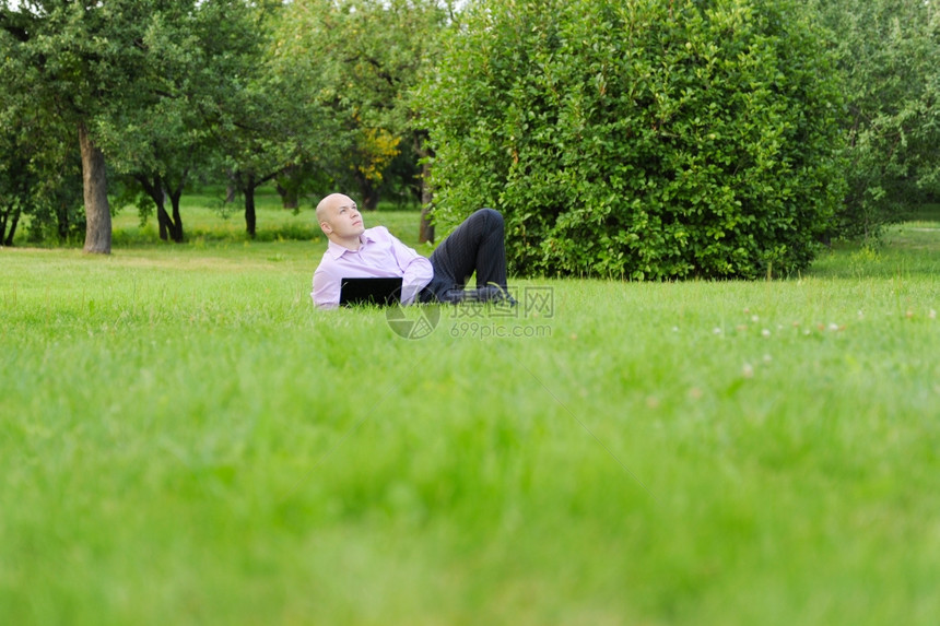 男人用笔记本电脑躺在公园绿草地上图片