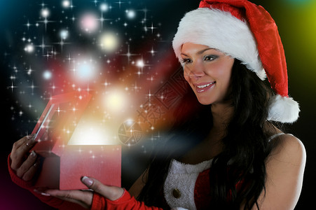 圣诞节甜美女性戴圣诞帽的妇女笑着在黑暗背景上拿着魔法包装的礼物设计图片