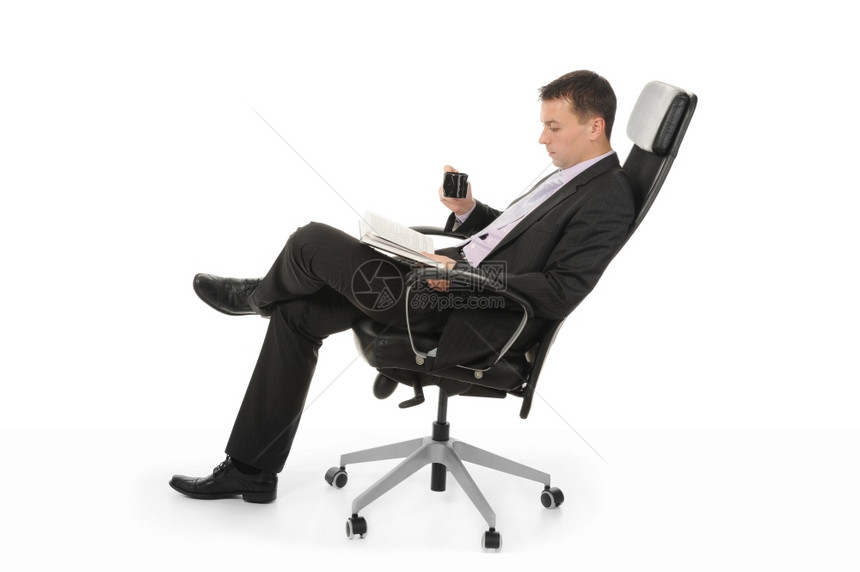商人阅读一本书喝咖啡坐在办公室的椅子上坐在一个明亮的办公室椅子上图片