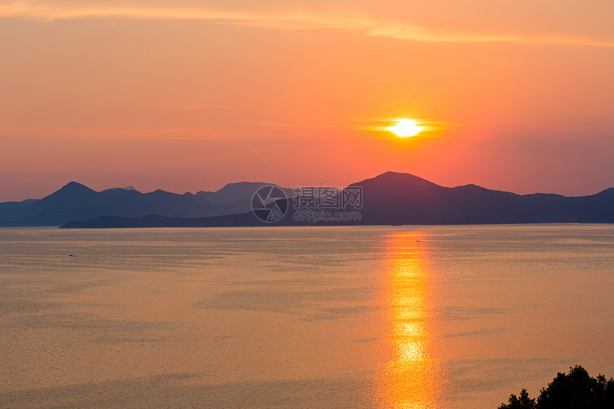 夏季傍晚海岸线有粉红黄色日落太阳轨道和地平线上的岛屿图片