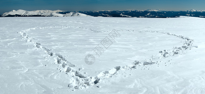 人类足迹在雪覆盖的山边高原和脉后面形成心脏状图片