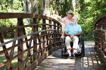 年长妇女用轮椅将残疾丈夫推过公园图片