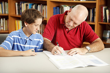 父亲在图书馆里帮助儿子做功课图片