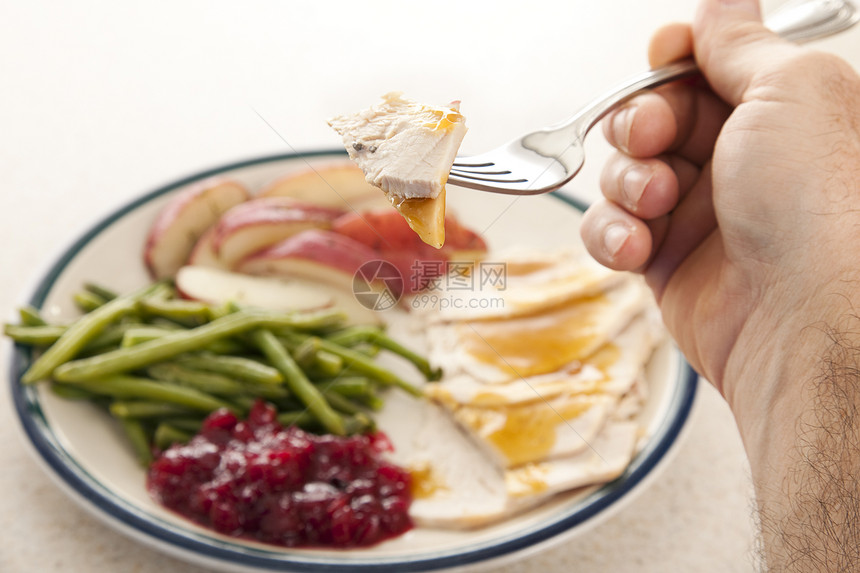 一个人的手握着叉子上面有火鸡一块将感恩节食物的盘子放在背景中将美国外交部的盘子放在了背景之下专注在单咬上图片