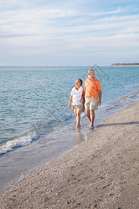 经济上安全的退休老年夫妇在美丽的海滩上散步图片