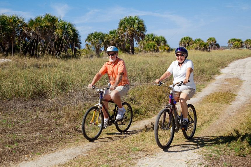 在海滩骑自行车的老夫妇戴安全头盔和墨镜图片