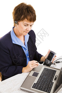 商业妇女将数据从她的PDA传送到她的笔记本电脑上图片