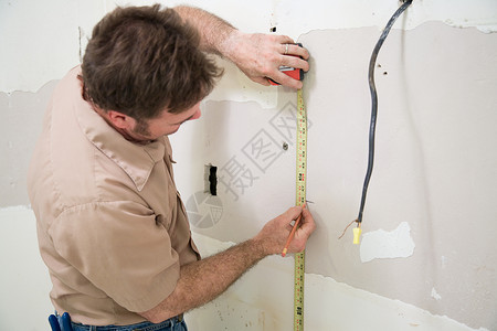 承包商测量和标记干墙想切断一个电箱的开口图片