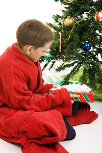 小男孩在树下打开圣诞礼物白色背景图片