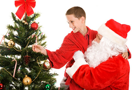 圣诞老人把一个小男孩抬起来从圣诞树顶上拿根糖果杖白色背景图片