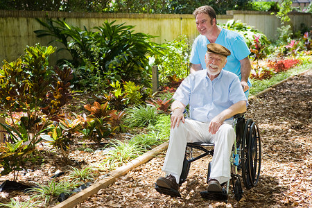 残疾老年男子被护士推过可爱的花园图片