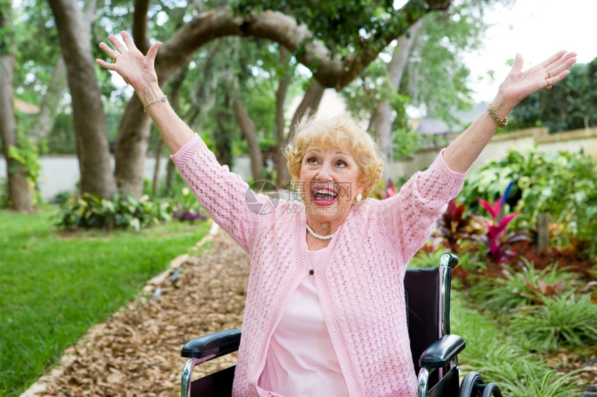 坐在轮椅上的高级女士在庆祝免于痛苦的自由时很欣喜图片
