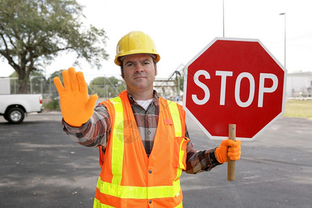 一个建筑工人持有停站的标志并指挥交通图片