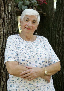 一位迷人的老祖母靠在一棵树上手折着的双臂图片