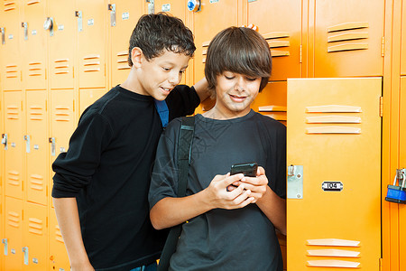 两个十几岁的男孩在学校储物柜旁玩手持电子游戏图片
