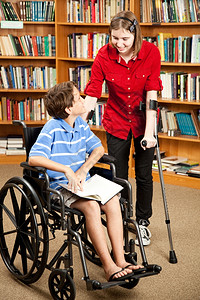 有前臂拐杖的残疾青少年与坐在轮椅上的小男孩交谈他们在图书馆图片