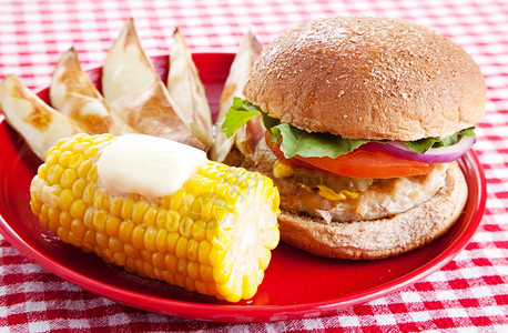 健康的火鸡汉堡放在一整包的谷物面上烤土豆和玉米在鳕鱼上红白的桌布图片