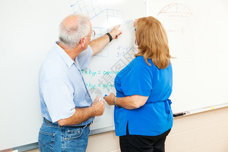 成人教育学生在老师的帮助下在董事会上做数学方程式工作图片