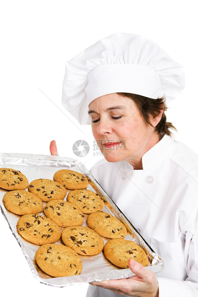 穿着制服的漂亮成熟女厨师吸入着她新鲜烤巧克力饼干的盘子芳香图片