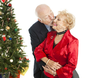 穿着节日服装的老年夫妇他亲吻她的脸颊背着圣诞树孤立无援图片