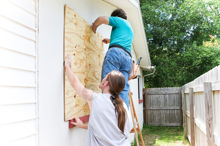 少年儿子帮助父亲把房的窗户套上为飓风或龙卷作准备图片