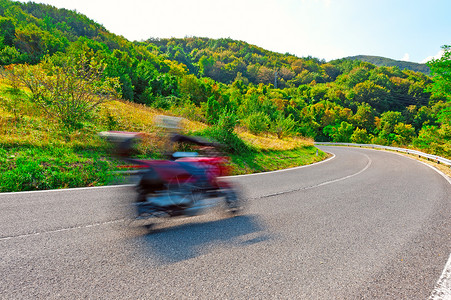 在意大利阿尔卑斯山的刮风灰尘路上运动模糊的摩托车手图片