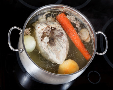 电炖盅在玻璃陶瓷锅炉上用钢里煮鸡汤和调味蔬菜背景