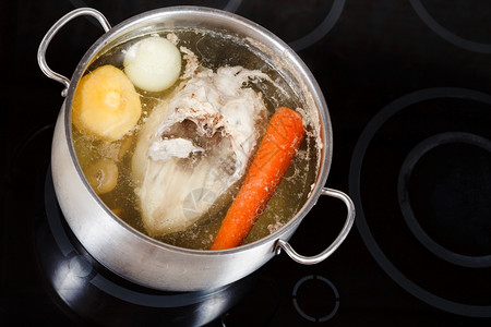电炖盅煮鸡汤在玻璃陶瓷锅炉上用钢里调制蔬菜背景