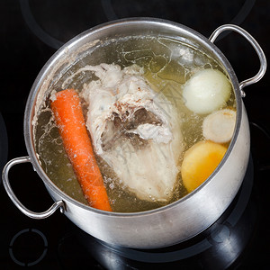 电炖盅在玻璃陶瓷锅炉上用钢筋煮鸡汤和调味蔬菜背景