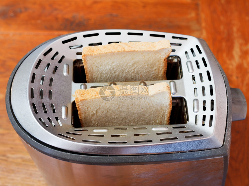 木制桌上金属烤面包机中的两片新鲜面包图片