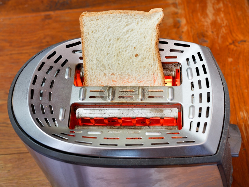 木制桌上热金属烤面包机上一小片新鲜面包图片