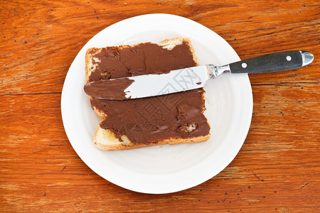 新鲜吐司的风景巧克力在白盘上撒布桌刀在木上图片