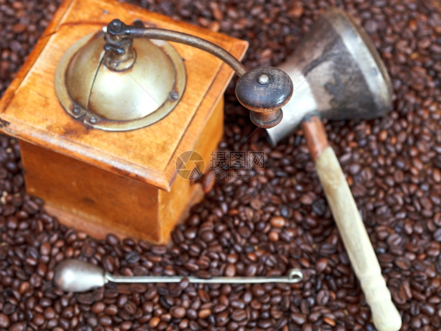 许多烤咖啡豆的回溯式手工咖啡研磨机和铜锅图片