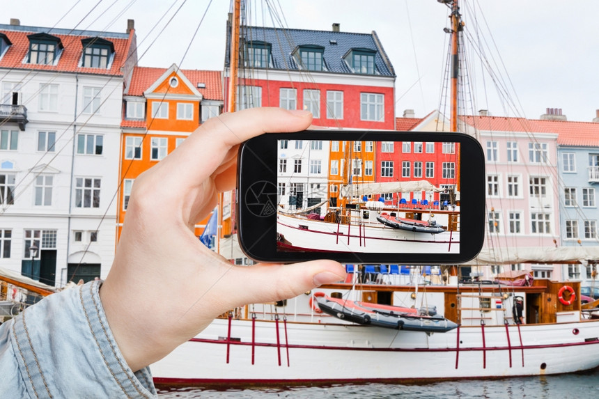 旅行概念在丹麦哥本哈根的Nyhavn水边运河和娱乐区用移动工具拍摄照片的游客图片