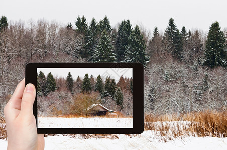 旅行概念旅游者在寒冷冬季用智能手机拍摄雪林边缘的低木屋图片