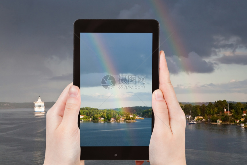 旅行概念旅游者用智能手机拍摄瑞典波罗的海沿岸小村庄上空的彩虹图片