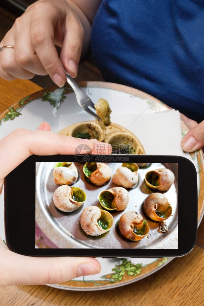 摄影食品概念旅游者拍摄热盘的埃斯卡戈贝壳在智能手机上配有特别的拖把和叉子图片