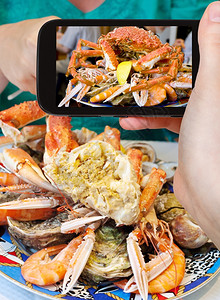 拍照食品概念旅游者用蟹虾和智能手机拍摄海鲜盘法国图片
