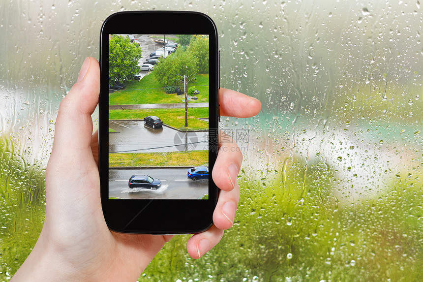 旅行概念旅游者用智能手机从家窗口拍摄城市淋浴的照片图片