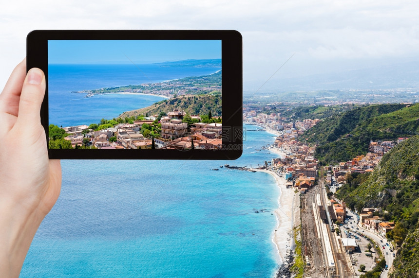 旅行概念游客用平板电脑拍摄意大利西里Taormina市伊奥尼亚海岸线和GiardiniNaxos镇的照片图片