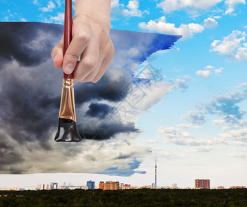 自然概念季节和天气变化手与油漆刷城市上空的黑风暴云图片