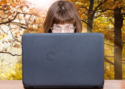 带着眼镜的女孩看露天笔记本电脑的封面秋天风景背图片