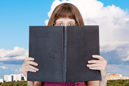 带着眼镜的女孩看着大书上面有空白的封城市周围的白云图片